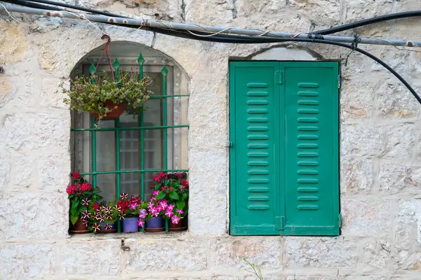 Stock image Green metal shutters and flowers in an arched window in a stone wall, typical of houses in old Jerusalem, Israel.