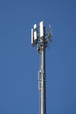 Üzerinde mavi gökyüzü tarafından çerçevelenmiş çeşitli antenler bulunan bir iletişim direği..