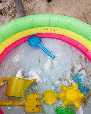 Şişme yüzme havuzu, su ve kumdaki oyuncaklar.