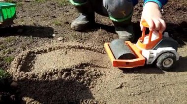 Bir çocuk kumdaki oyuncak sıkıştırıcıyla oynuyor.