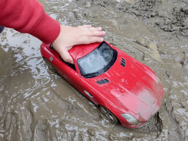 泥の中で赤いおもちゃの車と遊ぶ子供 — ストック写真
