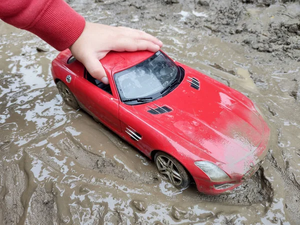 泥の中で赤いおもちゃの車と遊ぶ子供 — ストック写真