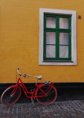 Red bike leaning against a yellow wall, with a green window behind and ample copy space. Copenhagen, Denmark. High quality photo clipart