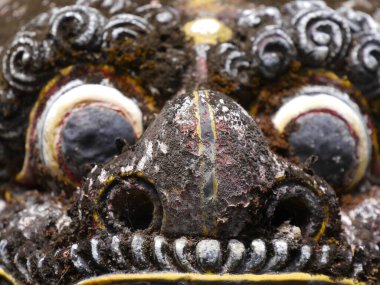 Close up of grotesque, scary face of statue of Balinese demon with staring eyes and fangs at Pura Sangara sea temple near Sanur. clipart