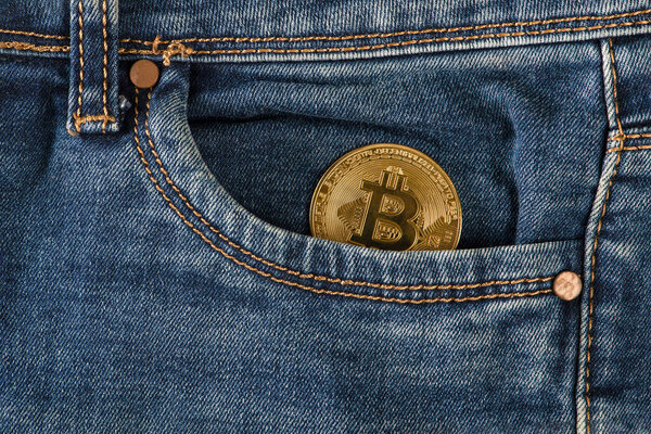 Bitcoin in your pocket. A golden bitcoin coin lies in the pocket of blue jeans. Salary in bitcoins, income in cryptocurrency