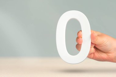 Sıfır numara elinde. Bir el, arka planı bulanık ve fotokopi alanı olan beyaz bir sıfırı tutar. Sıfır konsept, 0% faiz oranı, minimum hava emisyonu, maliyet veya kredi artış yok