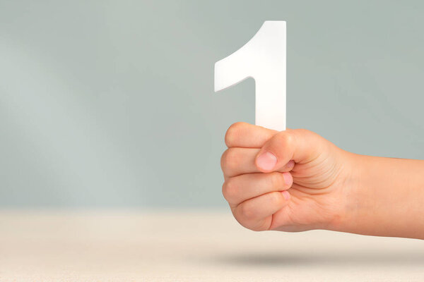 Number one in hand. A hand holds a white number one on a blurred background with copy space. Concept with number one. 1 percent rate, birthday, first or winner