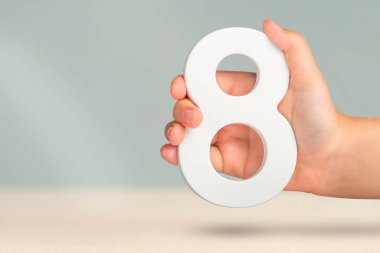 Eight in hand. A hand holds a white number 8 on a blurred background. Concept with number eight. Birthday 8 years, percentage, eighth grade or day, international womens day clipart