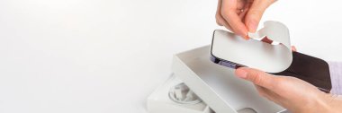 Unpacking a new phone. Remove the protective white film from the new phone. Close-up of a womans hands removing a protective film from a phone in a purple case. Copy space on white background