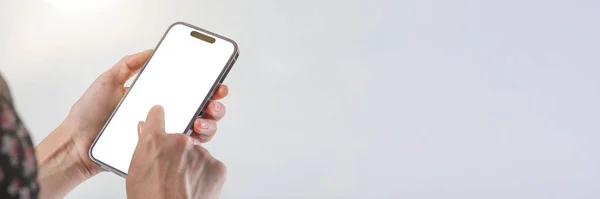 Phone in hand on a white background. A woman holds a phone in her hand on a white background and presses with her finger on a blank white screen. Finger tap on phone screen with copy space