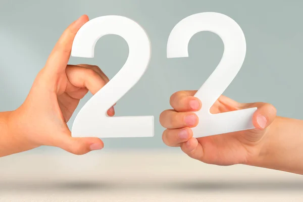 Number two two in hand. Hand holding white number 22 on blurred background with copy space. Concept with number twenty two. 22 percent, birthday 22, twenty two.