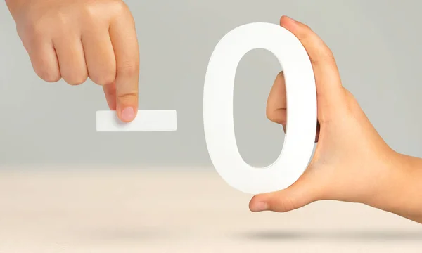 Minus zero. Numeral zero and minus symbol in a hand close-up on a light gray background. The concept of removal or taking away