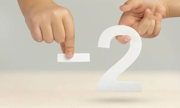Minus two. The number two and the minus symbol in a hand close-up on a light gray background. The concept of removal or taking away.