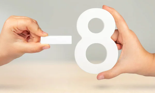 Minus eight. The number eight and the minus symbol in a hand close-up on a light gray background. The concept of removal or taking away.