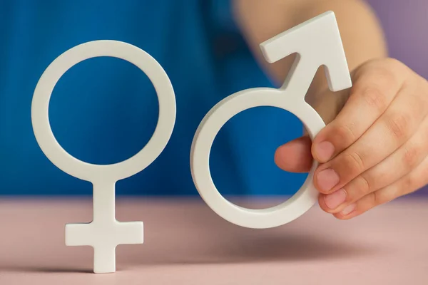 The concept of gender equality. Symbol of female and male gender in hand as a symbol of equality of rights. On a purple background in a blue t-shirt with copy space. High quality photo