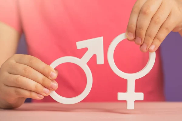 The concept of gender equality. Symbol of female and male gender in hand as a symbol of equality of rights. On a purple background in a pink t-shirt with copy space. High quality photo
