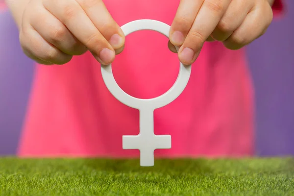 The concept of gender. Female gender symbol in hand on purple background in pink t-shirt with copy space. High quality photo