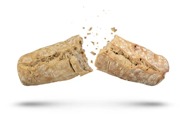 白い隔離された背景の2つの部分にイタリアの新鮮なシアバッタパンのローフが割られます Ciabattaパンは白い背景に隔離され パンくずは異なる方向に散布されます サイドビュー — ストック写真