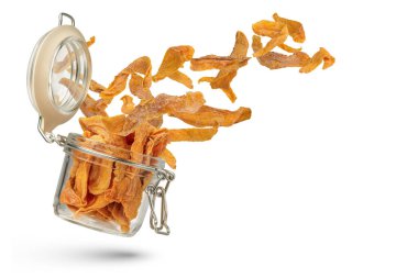 Beyaz izole bir arka planda cam bir kavanozda kurutulmuş mango. Kurutulmuş mango kavanozdan düşer. Mağazalara ya da üretime teslimat kavramı. Reklam afişi veya bir projeye eklenmeye uygundur