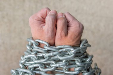 İşçi elleri, kölelik ya da bağımlılık kavramı olarak bir zincire sarılır. Gri arka planda zinciri olan bir kölenin ellerinin yakın plan fotoğrafı. Tutuklama ya da tutuklama