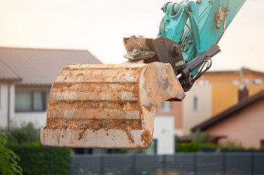 Yol tamiri. Kazıcı, birikmiş toprağı asfaltın olmayacağı bir yere boşaltıyor. Evlerin arka planında bir kazıcı ile toprağı kazma işlemi
