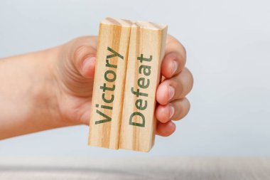 Zafer ve yenilgi. Bir el, bir tasarım veya projeye eklemek için üzerinde VICTORY ve DEFEAT yazıları olan iki tahta küpü tutar. Yüksek kalite fotoğraf