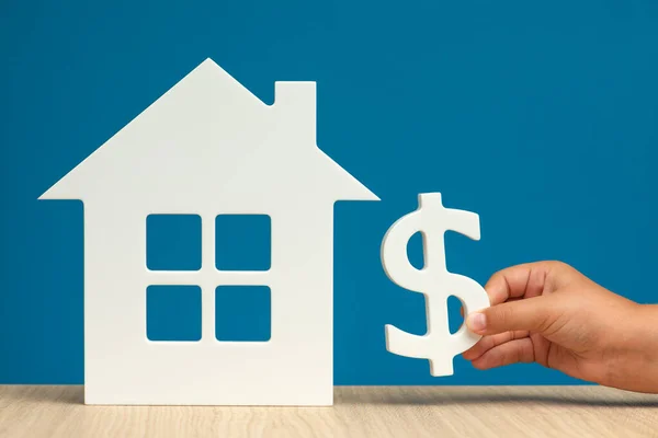 The cost of renting real estate in the USA. Renting residential real estate in America. Model of a white house and a hand with a dollar symbol on a blue background close-up. copy space.