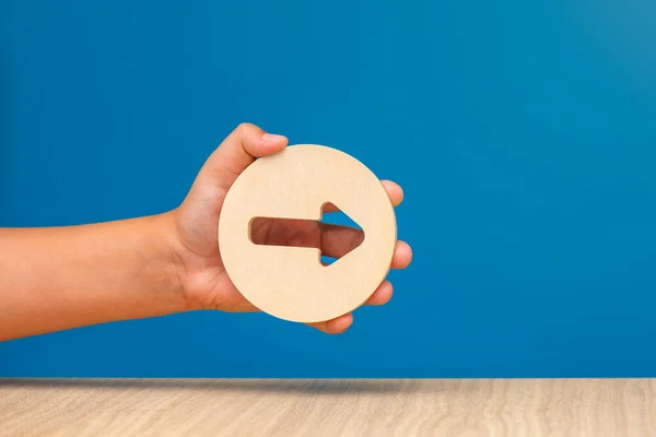 Arrow pointing right on a blue background. Banner with an arrow in a wooden circle in a hand close-up pointing to the right with copy space. High quality photo