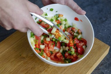 Salatayı karıştırma süreci. Salata karışımını karıştıran bir adamın yakın çekimi. Eller salatayı karıştırır, böylece malzemeler tabağa dağılır. Yüksek kalite fotoğraf