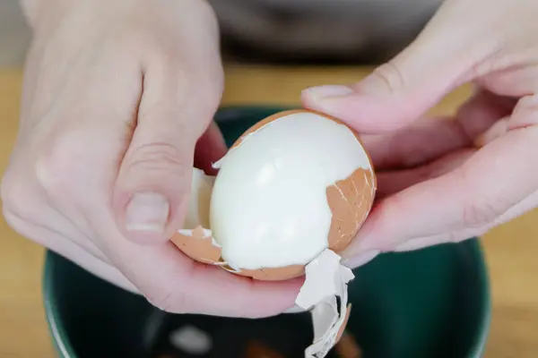A womans hand peels a boiled egg, removing the shell close-up. A quick snack in the form of a boiled egg. Top view. High quality photo