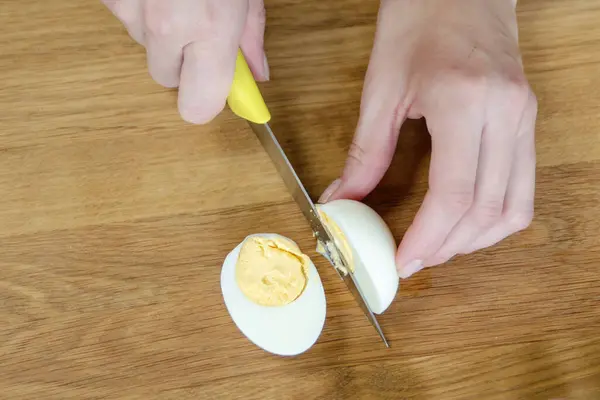 A womans hand cuts a boiled egg in half close-up. A quick snack in the form of a boiled egg. Top view. High quality photo