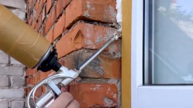 Pencere kurulumu. İnşaat köpüğüyle pencereleri yalıtma işlemi. Bir inşaatçı bina ile pencere çerçevesi arasındaki boşlukları elle kapatır. Bir binada pencere yalıtımı