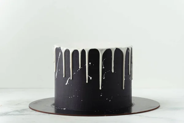 Black cake with white chocolate drips on the white background. Pouring chocolate on the cake. Chocolate drops on the cake