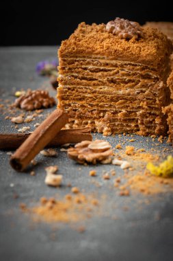 Gri beton arka planda ceviz ve tarçınlı geleneksel ballı pasta. Kare şeklinde, bal bazlı ve beyaz ekşi kremalı pasta..