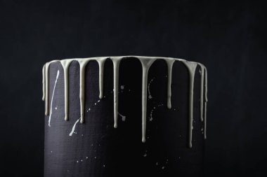 Siyah arka planda beyaz çikolata damlaları olan siyah pasta. Pastaya çikolata döküyorum. Pastanın üstüne çikolata damlası.