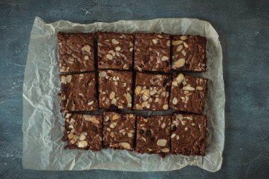 Lezzetli ev yapımı çikolatalı brovniler badem gevrekleri ve fırın parşömeninin üzerindeki kare dilimlere kesilmiş kuru üzümler. Düz yatıyordu. Gri beton arkaplan
