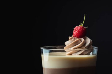 Ahududu ile süslenmiş katmanlı tatlı. Sünger bisküvisi ve üç çikolatalı mus tabakası. Tek kullanımlık şeffaf bardaklarda çikolatalı sufle keki. Siyah arkaplan