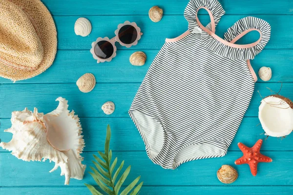 ビーチアクセサリー ヒトデ コココナッツの横にある子供用の1ピースの水着とわら帽子木製のターコイズの背景 夏の波と海の概念による休暇 — ストック写真