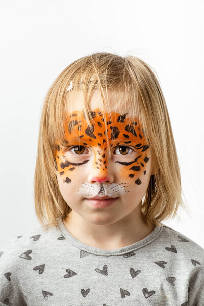 Cute little caucasian girl with tiger face painting on the white background. Close up portrait of little kid with face-painting. Year of a tiger. Happy smiling girl