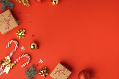 Karton hediye kutuları, baston şekerler ve altın Noel ağacı oyuncaklarıyla Noel arkaplanı. Yaklaşan tatillerin şenlikli hissi. Tebrik mesajı için kopyalama alanı olan kırmızı arkaplan. Düz yatıyordu