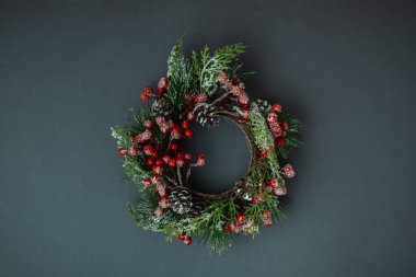 Kırmızı böğürtlenlerle süslenmiş Noel çelengi ve gri arka planda koni ile Noel arkaplanı. Düz yatıyordu. Bir ileti metni için alanı kopyala