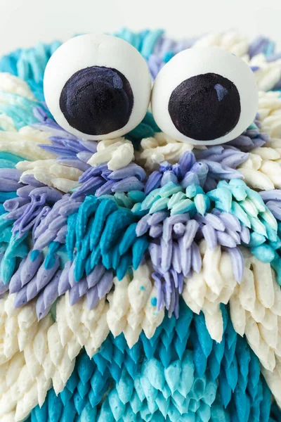 Cute monster cake on the white background. Funny birthday cake with turquoise and blue fluffy cream cheese frosting decorated with mastic edible eyes on top. Spooky kids Halloween party cake