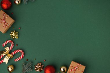 Karton hediye kutuları, baston şekerler ve altın Noel ağacı oyuncaklarıyla Noel arkaplanı. Yaklaşan tatillerin şenlikli hissi. Tebrik mesajı için fotokopi alanı olan koyu yeşil bir arkaplan. Düz yatıyordu