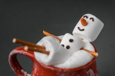 Marshmallow Kardan Adam süt köpüklü kakao dolu kırmızı seramik bir bardakta jakuziye giriyor. Noel tatilleri gri arka plan. Kış konsepti. Marşmelovlu ve şenlikli sıcak çikolata..