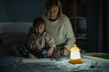 Anne ve küçük kızı elektrik kesintisi sırasında karanlıkta çalışıyor ve resim çiziyorlar. Küçük kız bilinç kaybı sırasında ev ödevini yapmak için kamp feneri kullanıyor. Enerji krizi kavramı