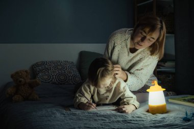 Anne ve küçük kızı elektrik kesintisi sırasında karanlıkta çalışıyor ve resim çiziyorlar. Küçük kız bilinç kaybı sırasında ev ödevini yapmak için kamp feneri kullanıyor. Enerji krizi kavramı