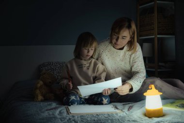 Anne ve küçük kızı elektrik kesintisi sırasında karanlıkta çalışıyor ve resim çiziyorlar. Küçük kız bilinç kaybı sırasında ev ödevini yapmak için kamp feneri kullanıyor. Enerji krizi kavramı