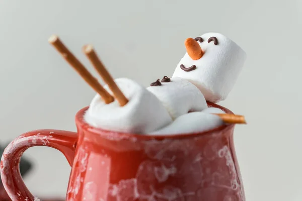 stock image Marshmallow snowman taking hot tub in a red ceramic cup full of cocoa with milk foam. Christmas holidays grey background. Wintertime concept. Hot chocolate with marshmallow and festive decoration.