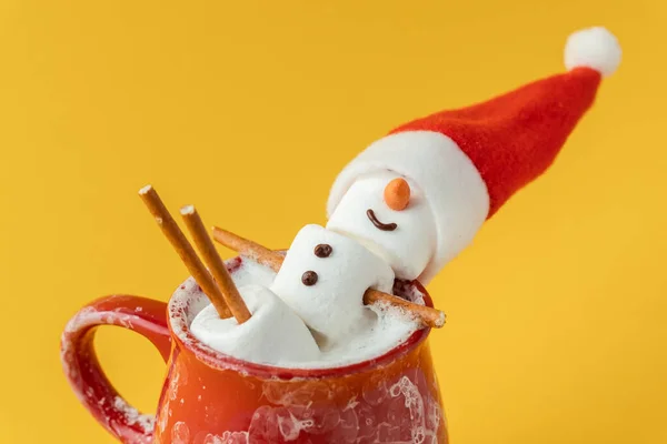 マシュマロスノーマンは ミルクフォームのココアが入った赤いセラミックカップでホットタブを取ることができます クリスマス休暇黄色の背景 冬のコンセプト ホットチョコレートマシュマロとお祝いの装飾 — ストック写真