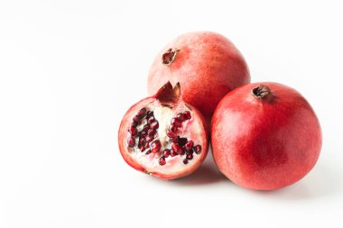 Beyaz arka planda izole edilmiş tam ve yarım taze nar meyvesi. Olgun narlar yarıya bölündü ve kırmızı sulu tohumlar sergilendi.